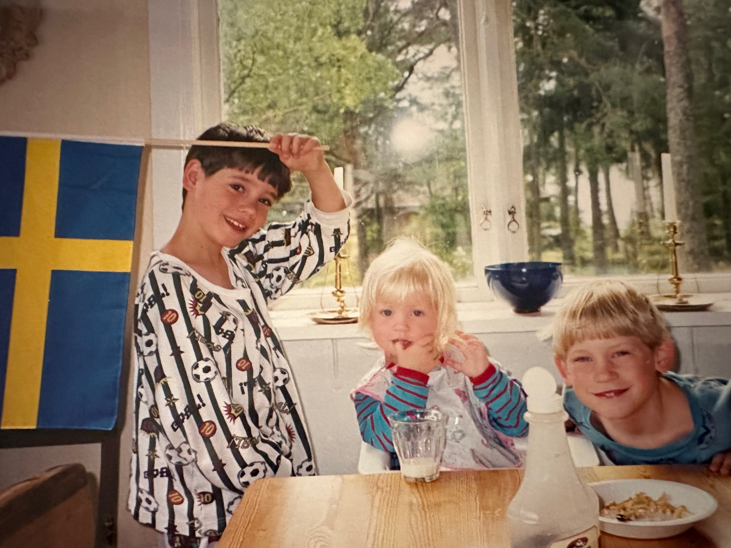 Three children sitting at a table with a Swedish flag  in hand