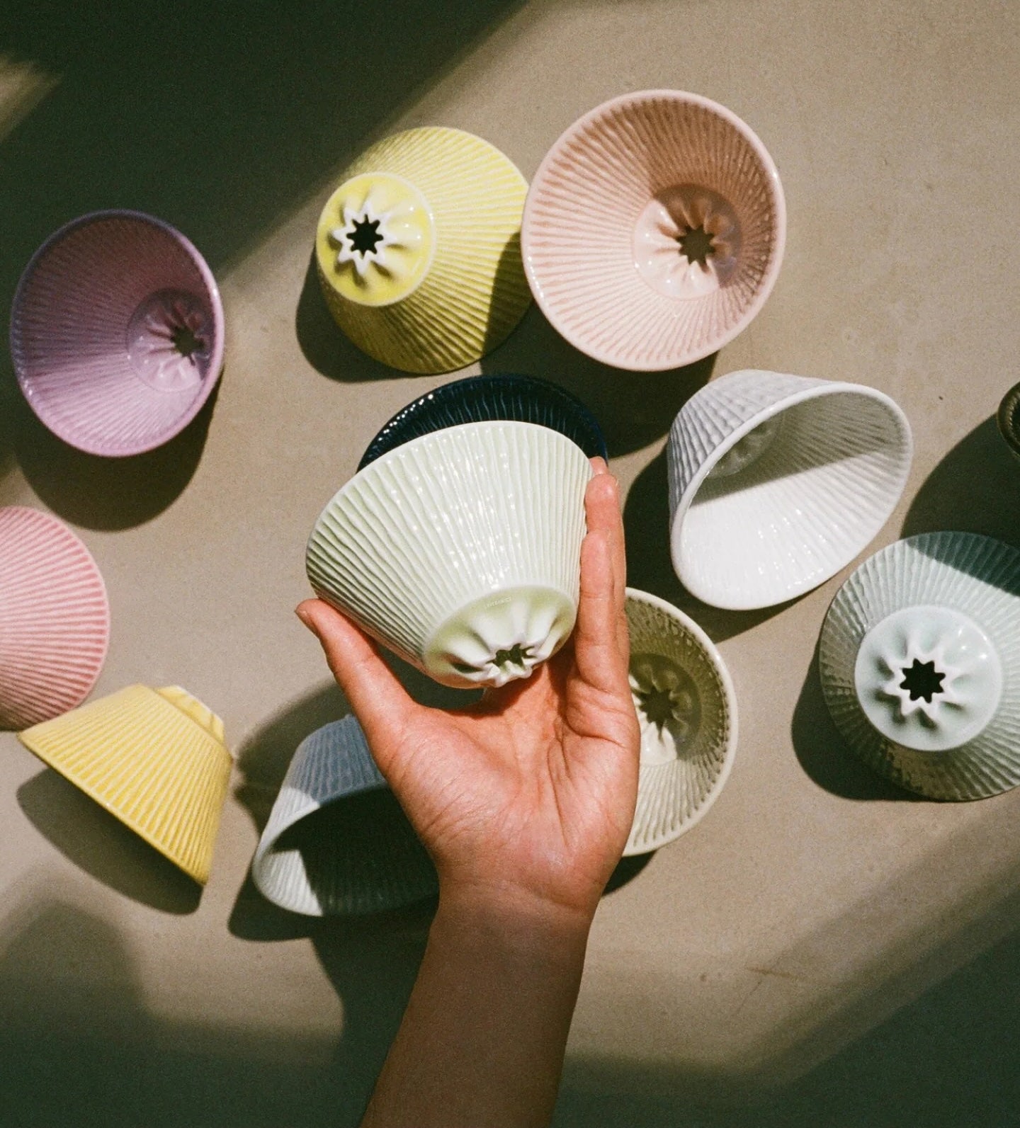 Hand holding a textured ceramic cup among other colorful ceramic cups on a neutral surface
